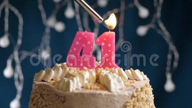 生日蛋糕，41个数字燃烧由较轻的粉红色蜡烛在蓝色的背面。 蜡烛被点燃了。 慢动作